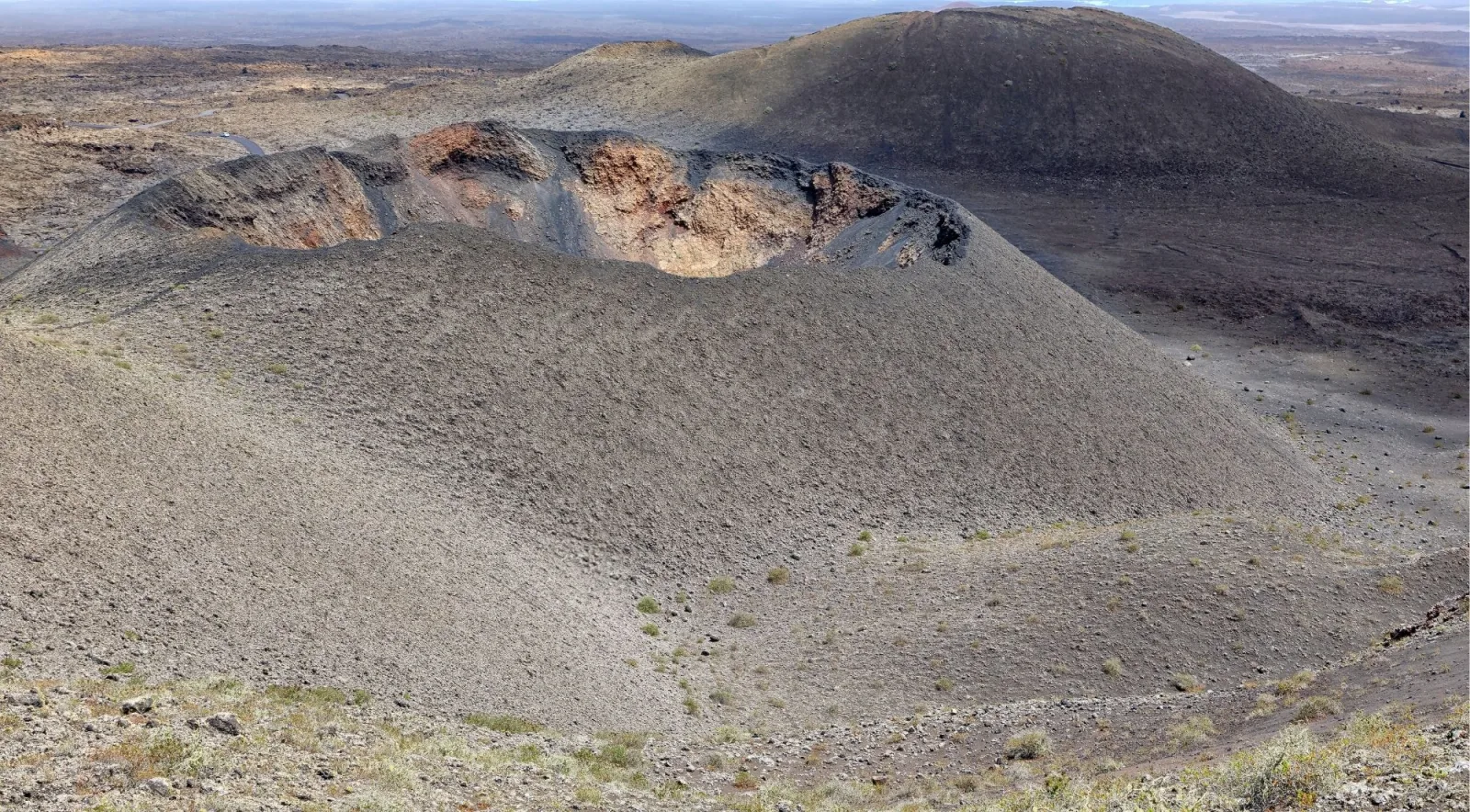 Aerial view of a grey ash cone with a breached crater rim exposing orange rock