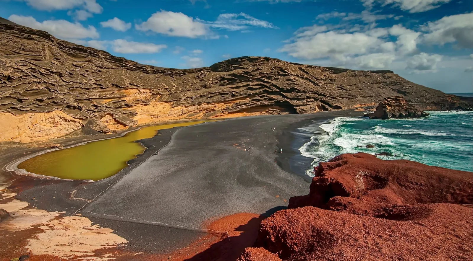 Red and ochre volcanic ridges above a wide plain of rust-coloured ash under a blue sky