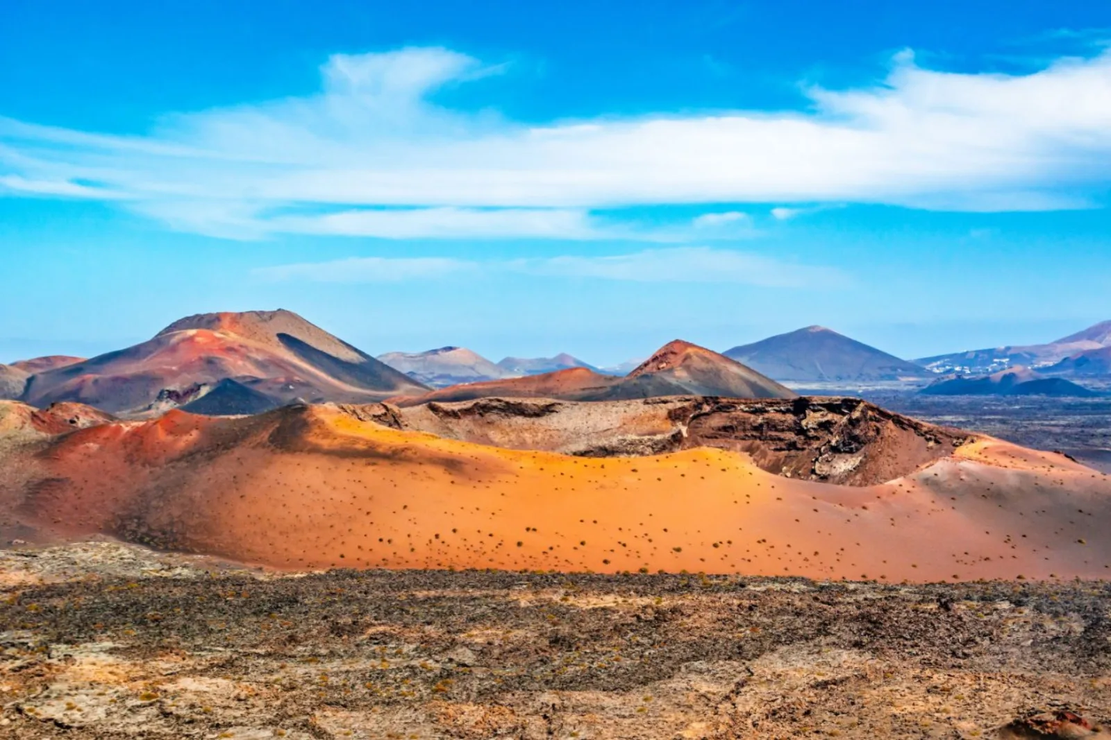 An orange-red cinder cone in bright sun with the wider crater field behind it