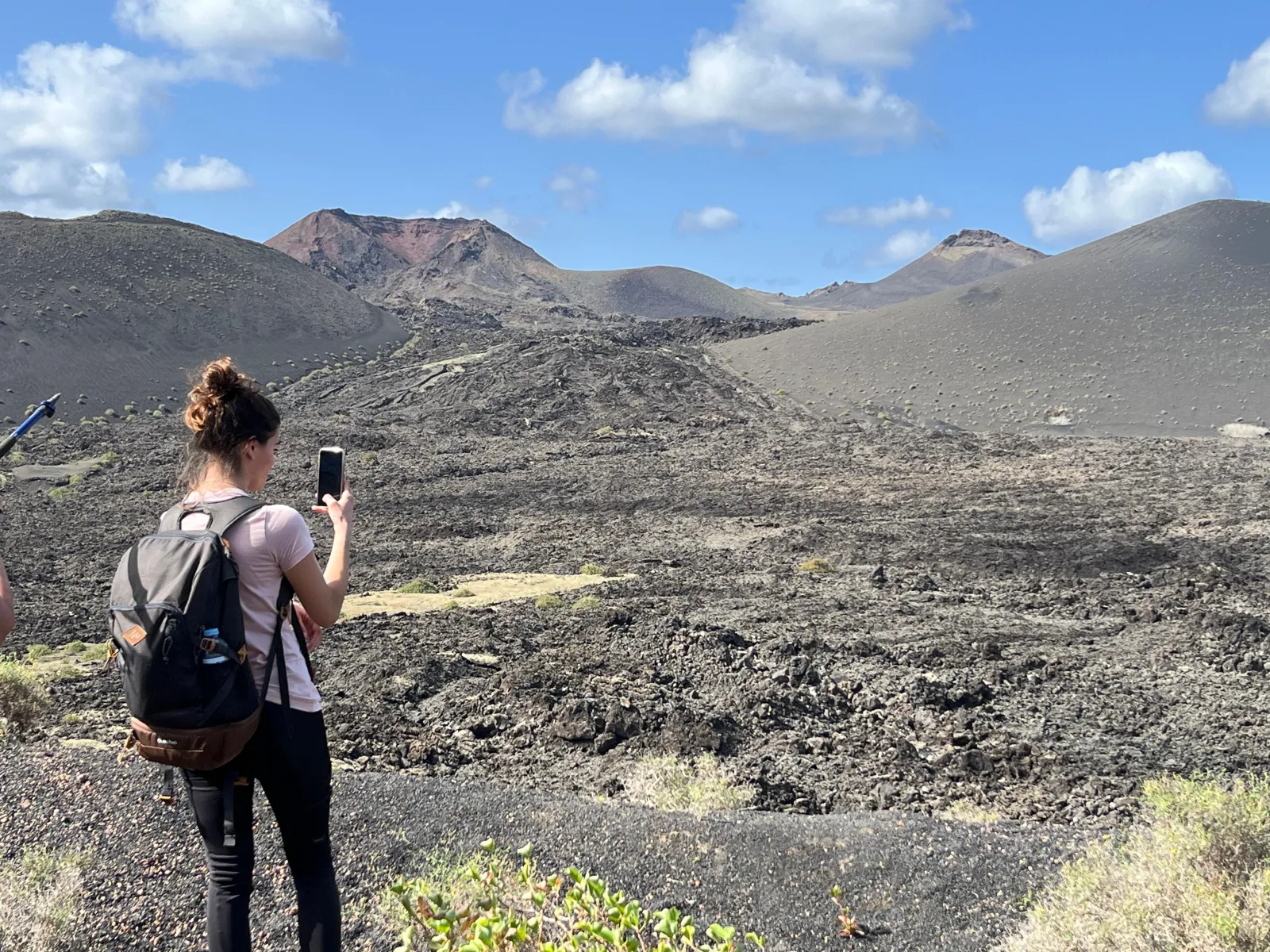 A hiker photographing the cones from the trail across the open lava field