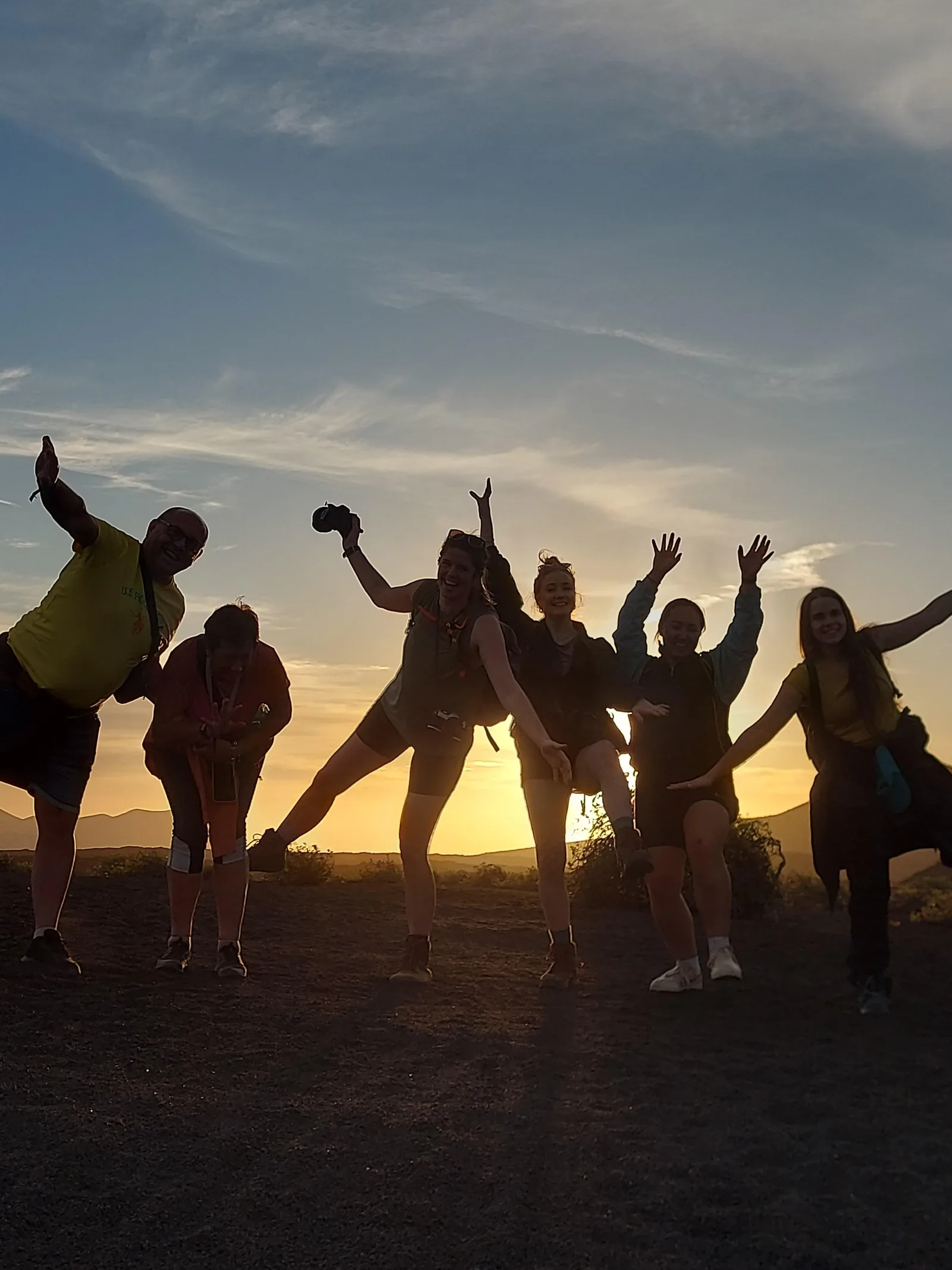 The group celebrating on the ridge line at sunset, arms raised against an orange sky