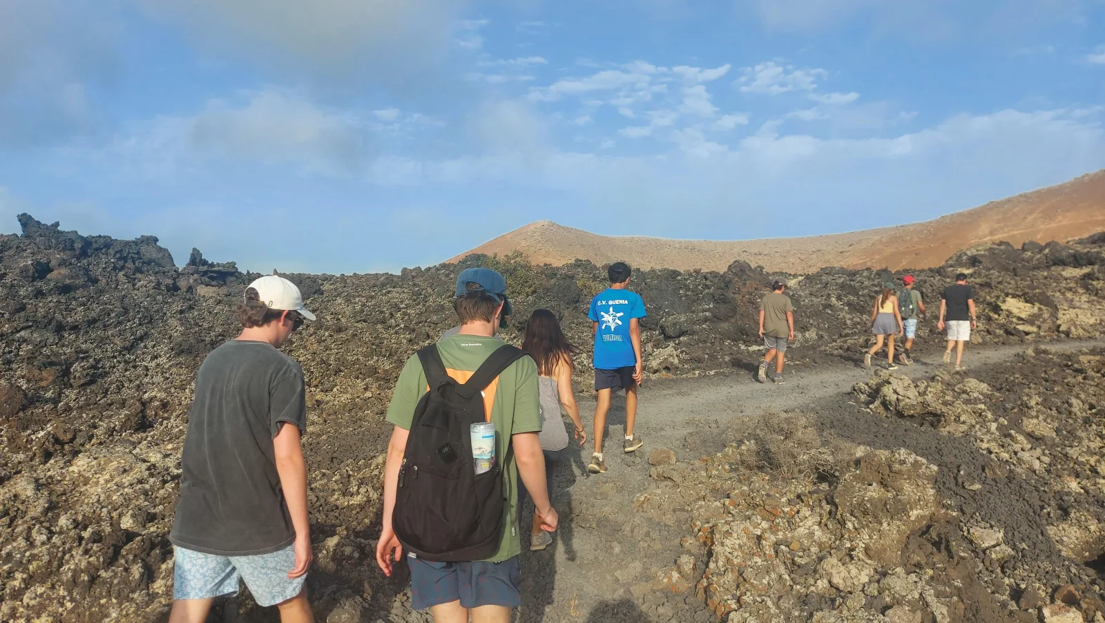 The group walking a stony trail between lava blocks with cones on the horizon