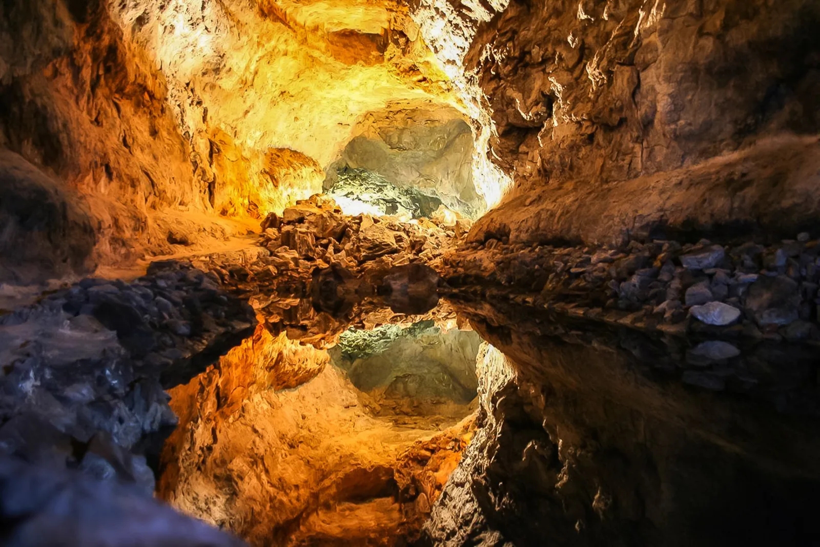 Sunlit orange rock inside the Cueva de los Verdes lava tube, mirrored in still water