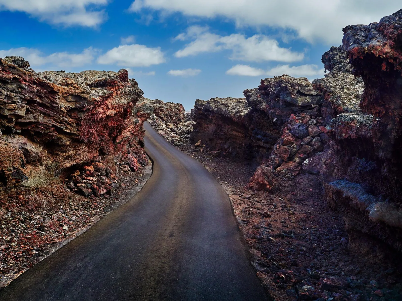 A narrow road cut through a corridor of dark red lava rock in the volcanic landscape