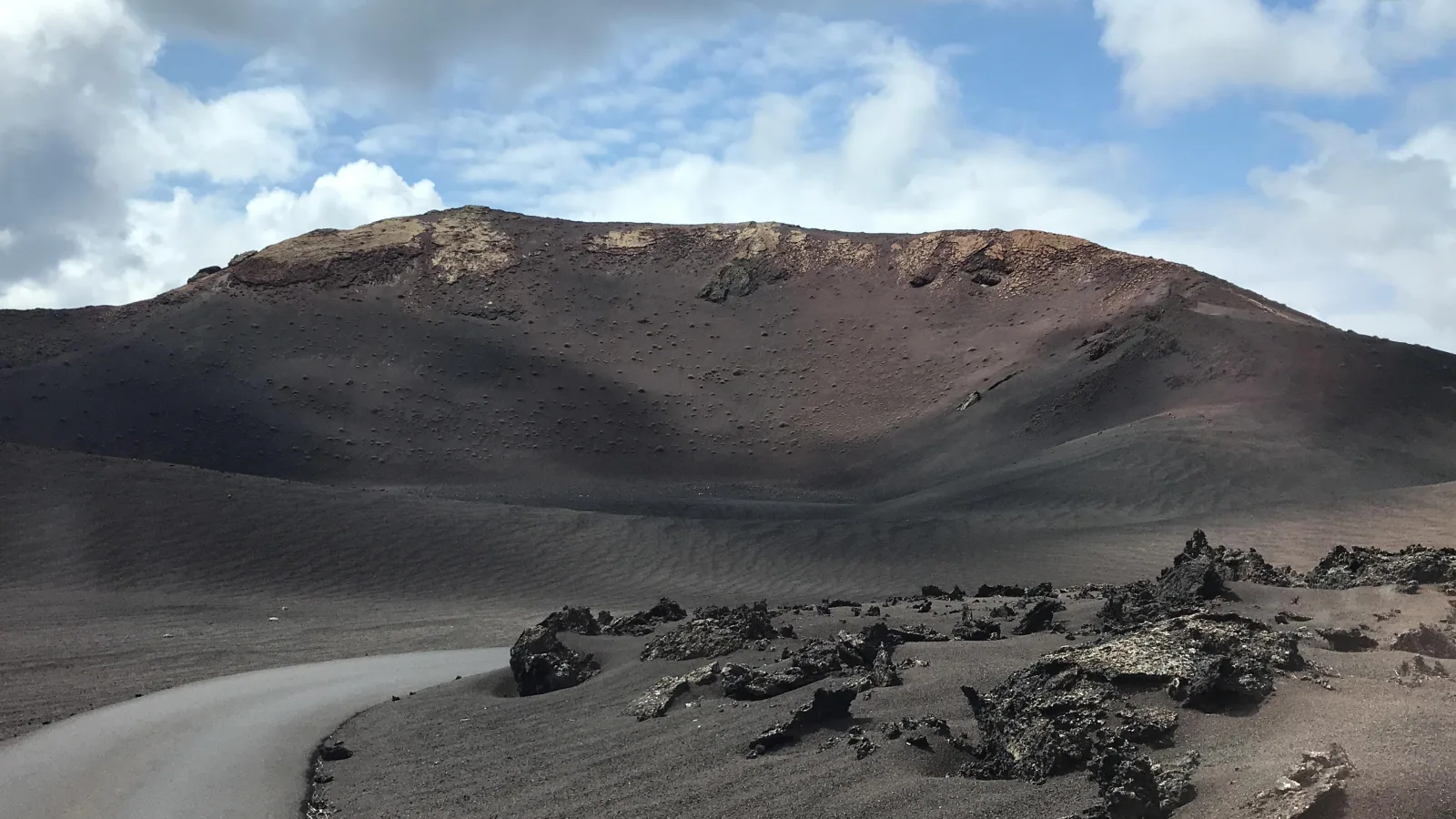 A broad grey cone with a deep breached crater above a black lava field