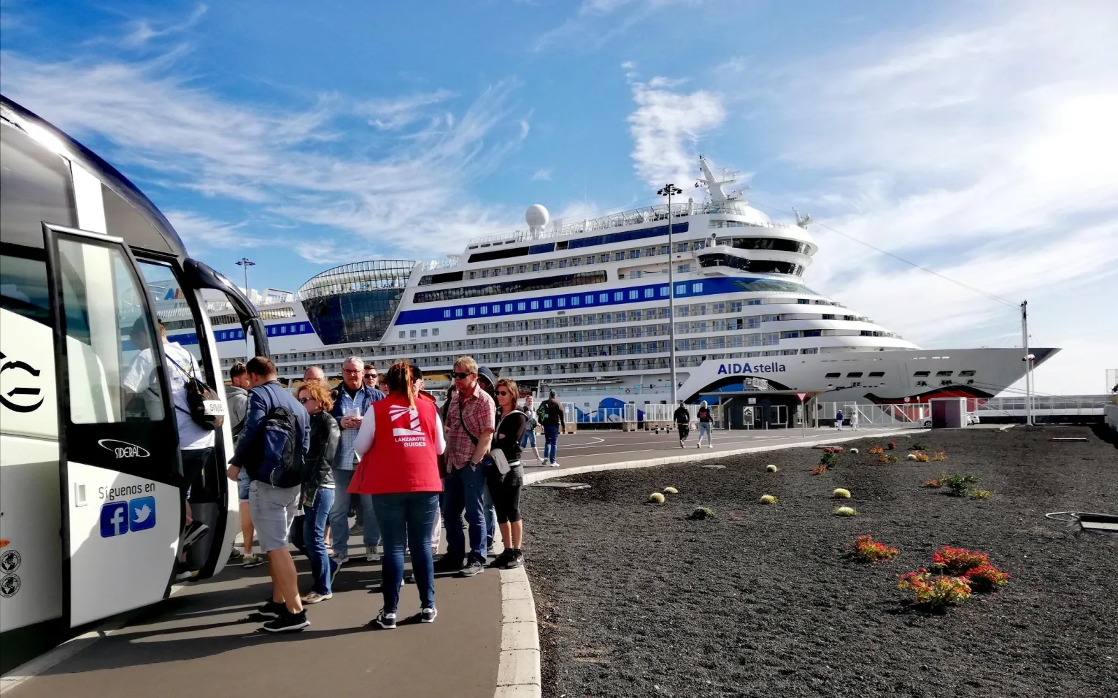 Tour passengers boarding a coach beside a docked cruise ship at Arrecife
