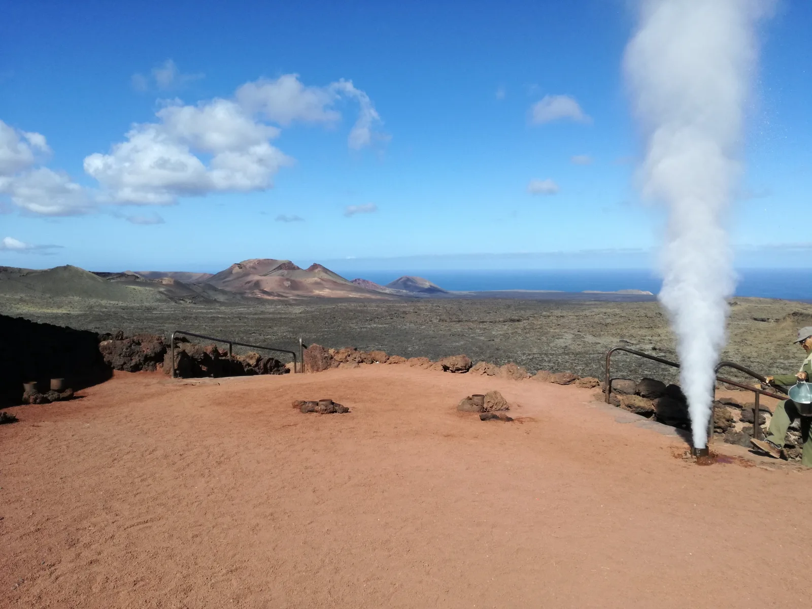 A column of steam firing from the ground at the Islote de Hilario above the red ash plain