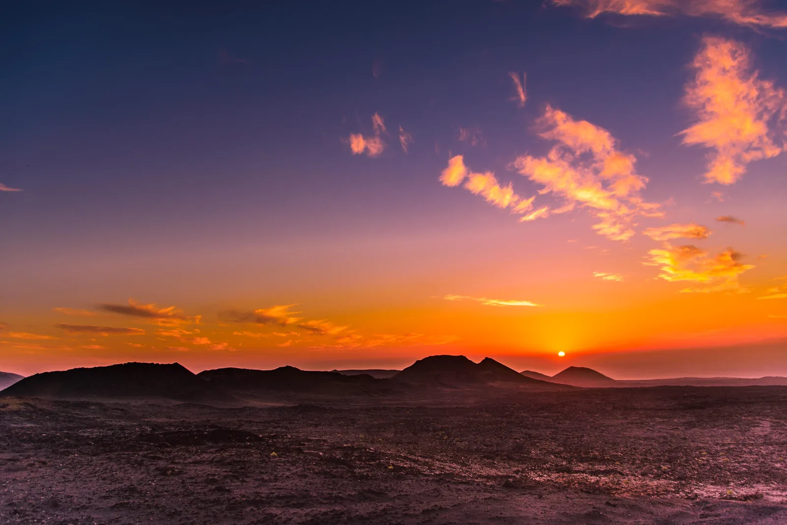 Sunset over the silhouetted cones of Timanfaya, the sky banded orange and violet